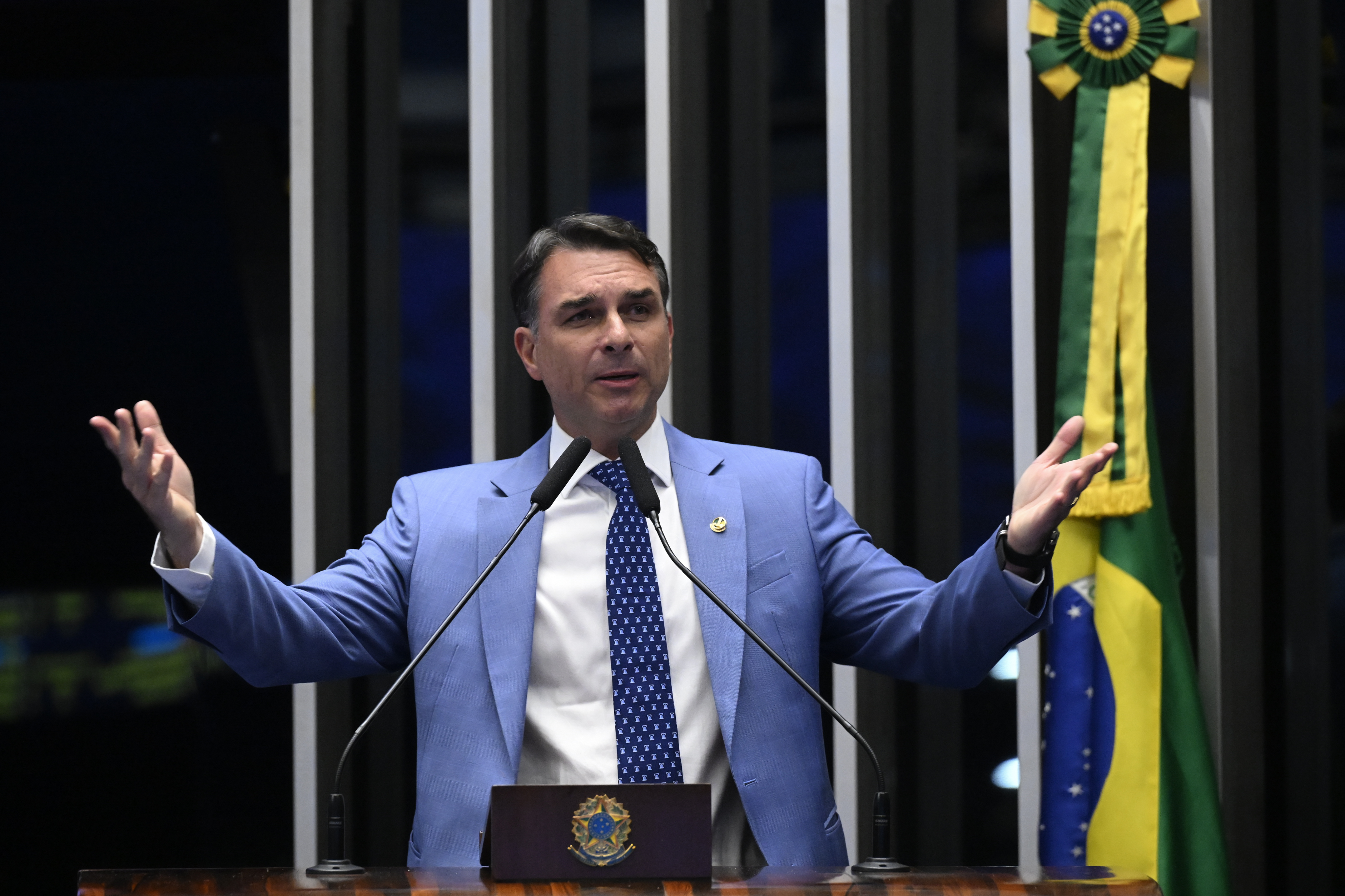 Flávio Bolsonaro discursa na tribuna do Senado, de terno azul, com a bandeira brasileira ao fundo. Foto de arquivo de 1º de setembro de 2026.